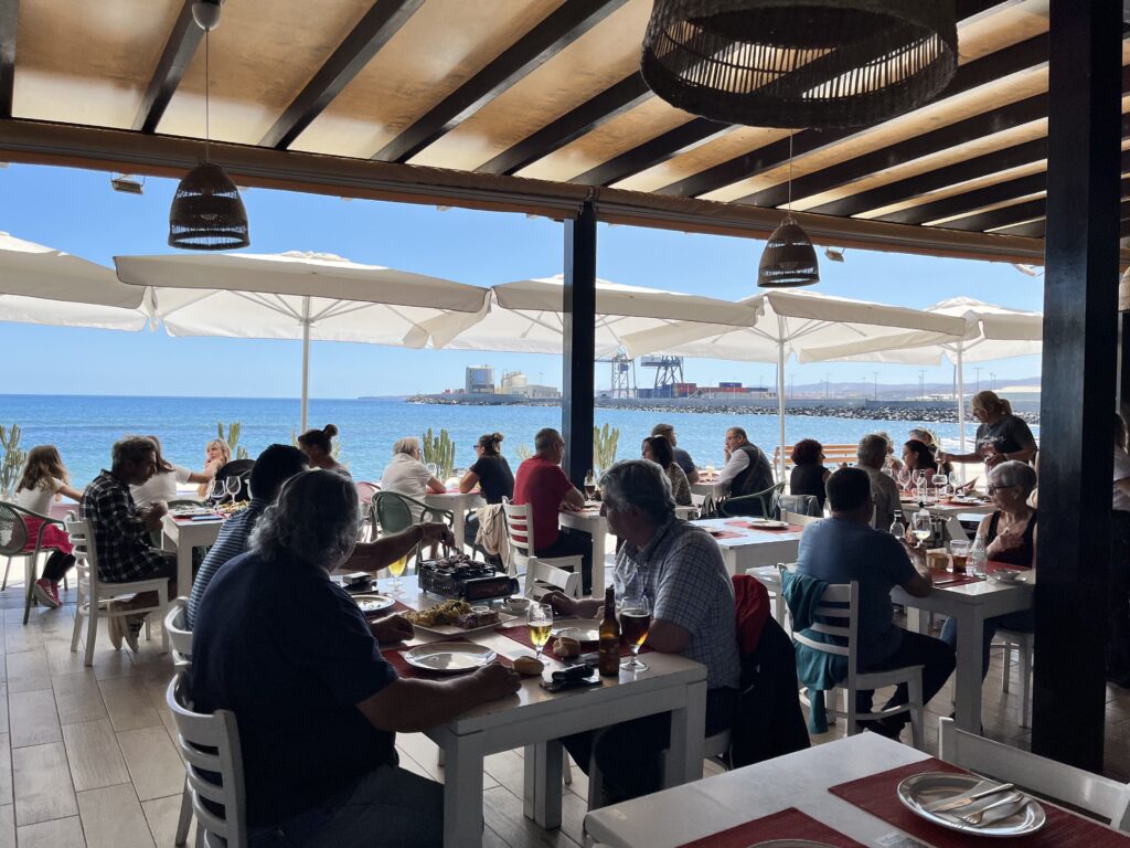 Clientes disfrutando en el comedor con la terraza abierta y el mar de fondo