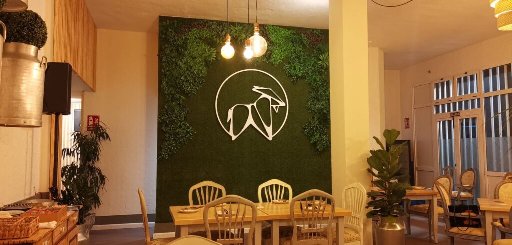 Pared de césped artificial con el logo blanco de La Puipana y mesa de comedor delante