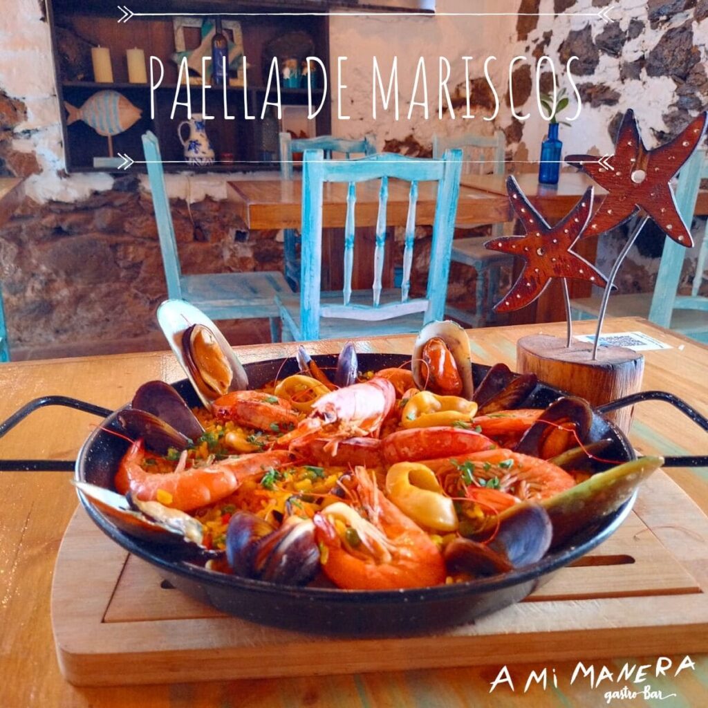 Paella de mariscos con gambas, mejillones y calamares servida en paellera sobre mesa de madera.