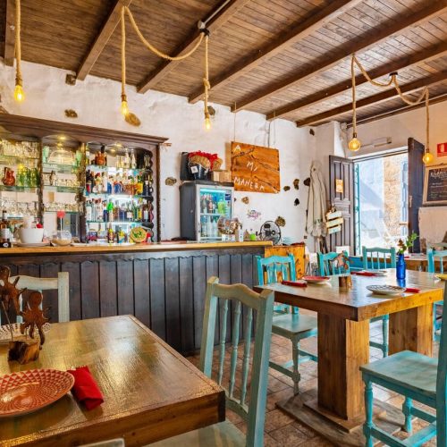 Primer plano de mesa con vajilla y al fondo la barra con copas y botellas en A Mi Manera.