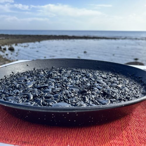 Paella de arroz negro servida en paellera con vista al mar en Fuerteventura