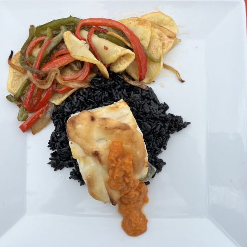 Lomo de bacalao con salsa sobre arroz negro, pimientos salteados y papas