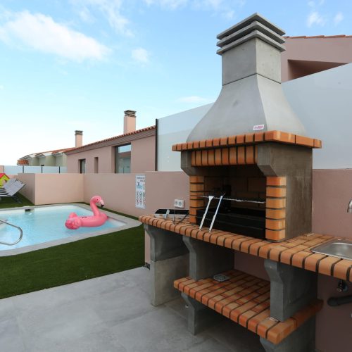 Barbacoa de ladrillo vista y encimera con fregadero frente a la piscina