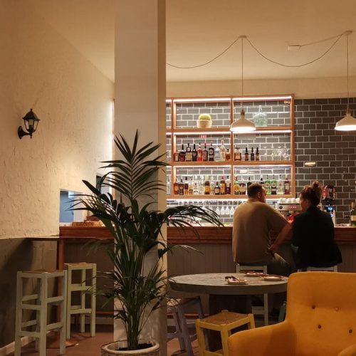 Barra de La Puipana con contrabarra de ladrillo negro, botellero iluminado y clientes sentados.