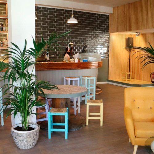 Vista general de la barra con plantas, mesas bajas y butaca amarilla en La Puipana