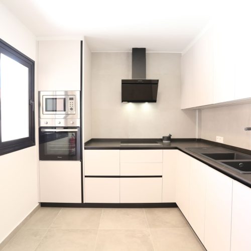 Cocina blanca con encimera negra, horno y microondas integrados en Villa Picasso