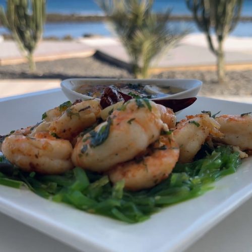 Gambas salteadas con ajo y guindilla sobre cama verde, con salsa al fondo