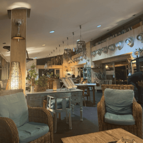 Sillones de mimbre con cojines azul verdoso, mesas de madera, lámparas colgantes y plantas en el interior del Restaurante Algo Más en Caleta de Fuste.