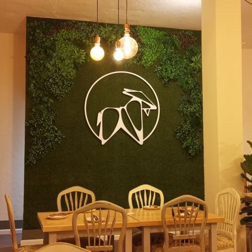 Pared de césped artificial con el logo blanco de La Puipana y mesa de comedor delante