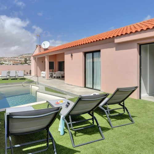 Piscina junto a jardín artificial con hamacas y fachada en tonos rosados