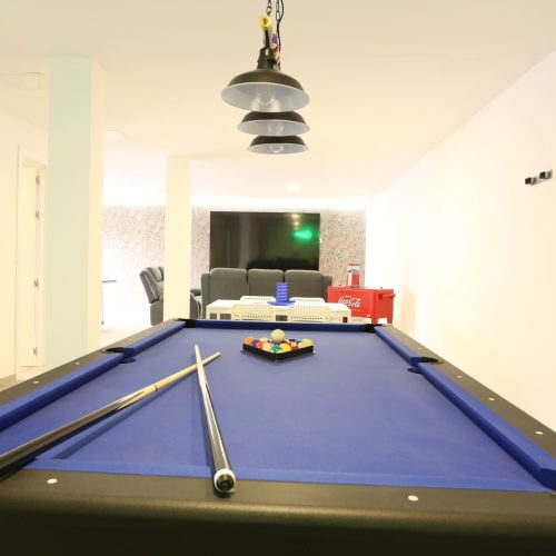 Mesa de billar azul con zona de sofás y pantalla grande al fondo