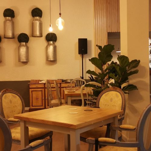 Comedor de La Puipana con sillas tapizadas, lecheras decorativas en pared y logo sobre pared vegetal.