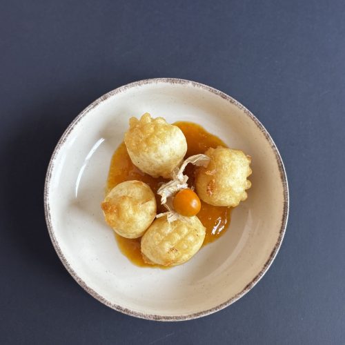 Bolitas fritas de La Puipana servidas en plato con salsa naranja y physalis