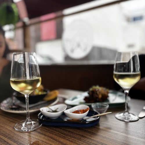 Dos copas de vino blanco y platos de tapas en terraza de La Puipana